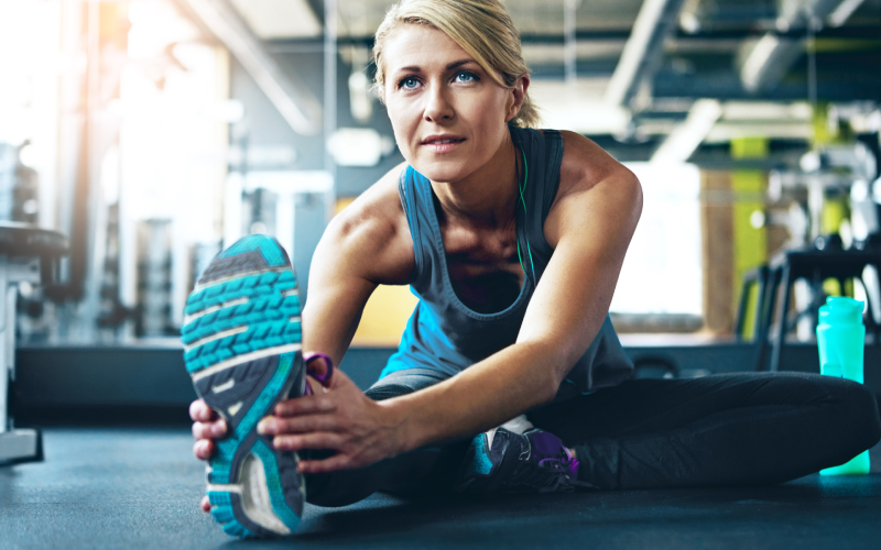 Woman stretching in gym, wearing blue shoes.